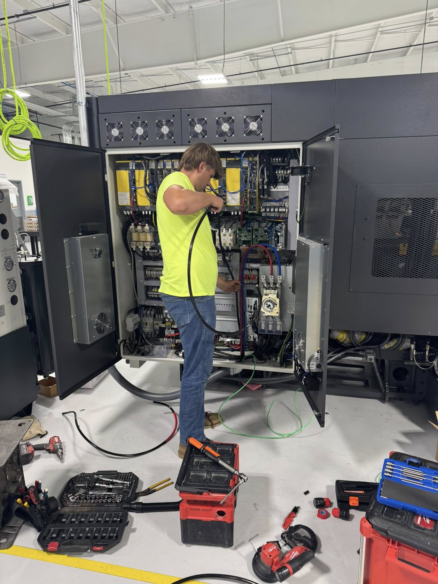 Commercial electrician in Southington, CT working on industrial electrical panel wiring inside a manufacturing facility, surrounded by tools and equipment.