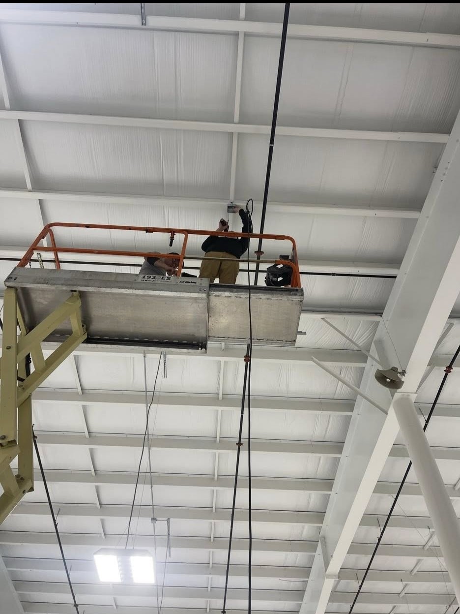 Commercial electricians in Southington, CT installing overhead electrical wiring from a lift inside a large industrial facility.