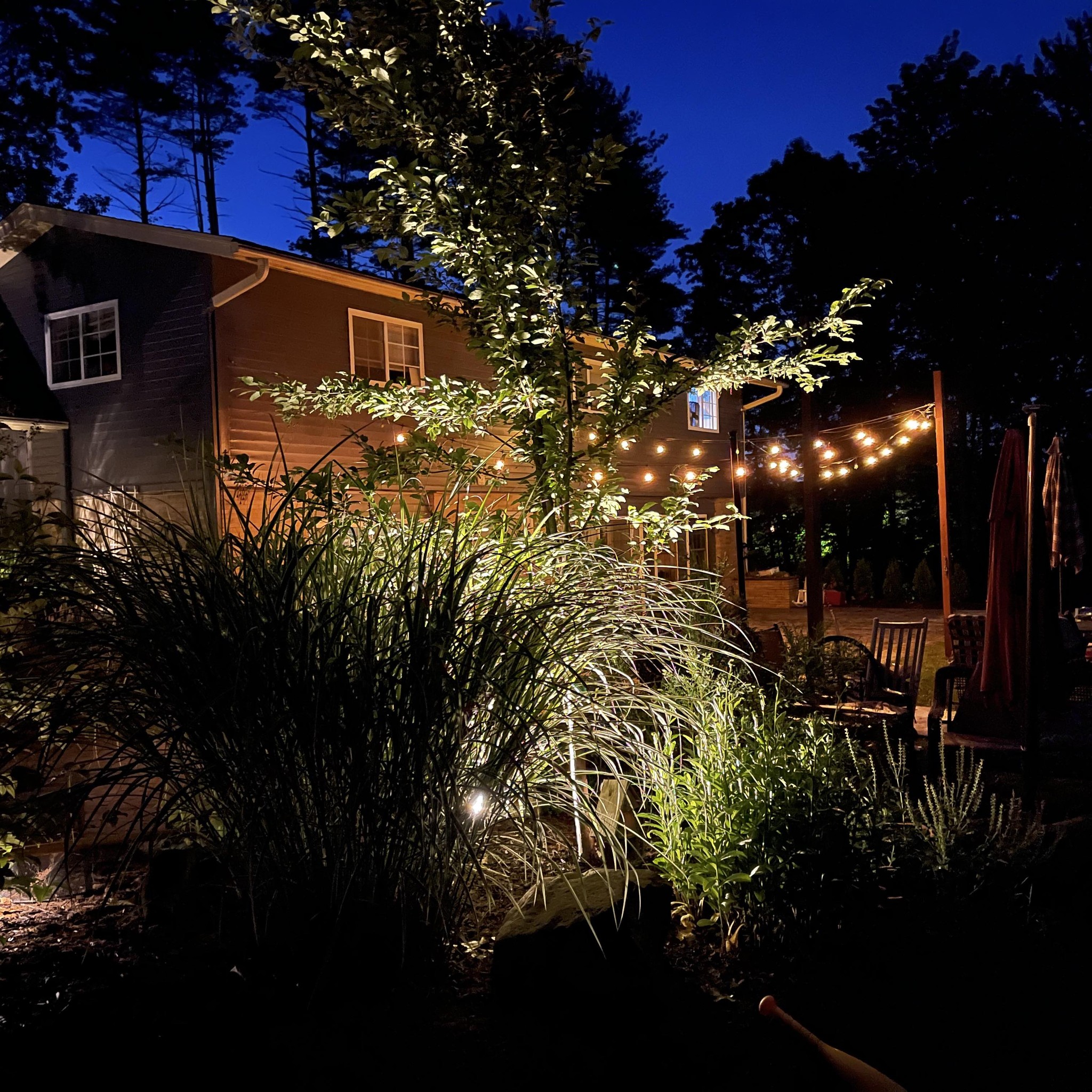 Outdoor residential backyard at night featuring string lights, illuminated landscaping, patio furniture, and a two-story house in Southington, CT.